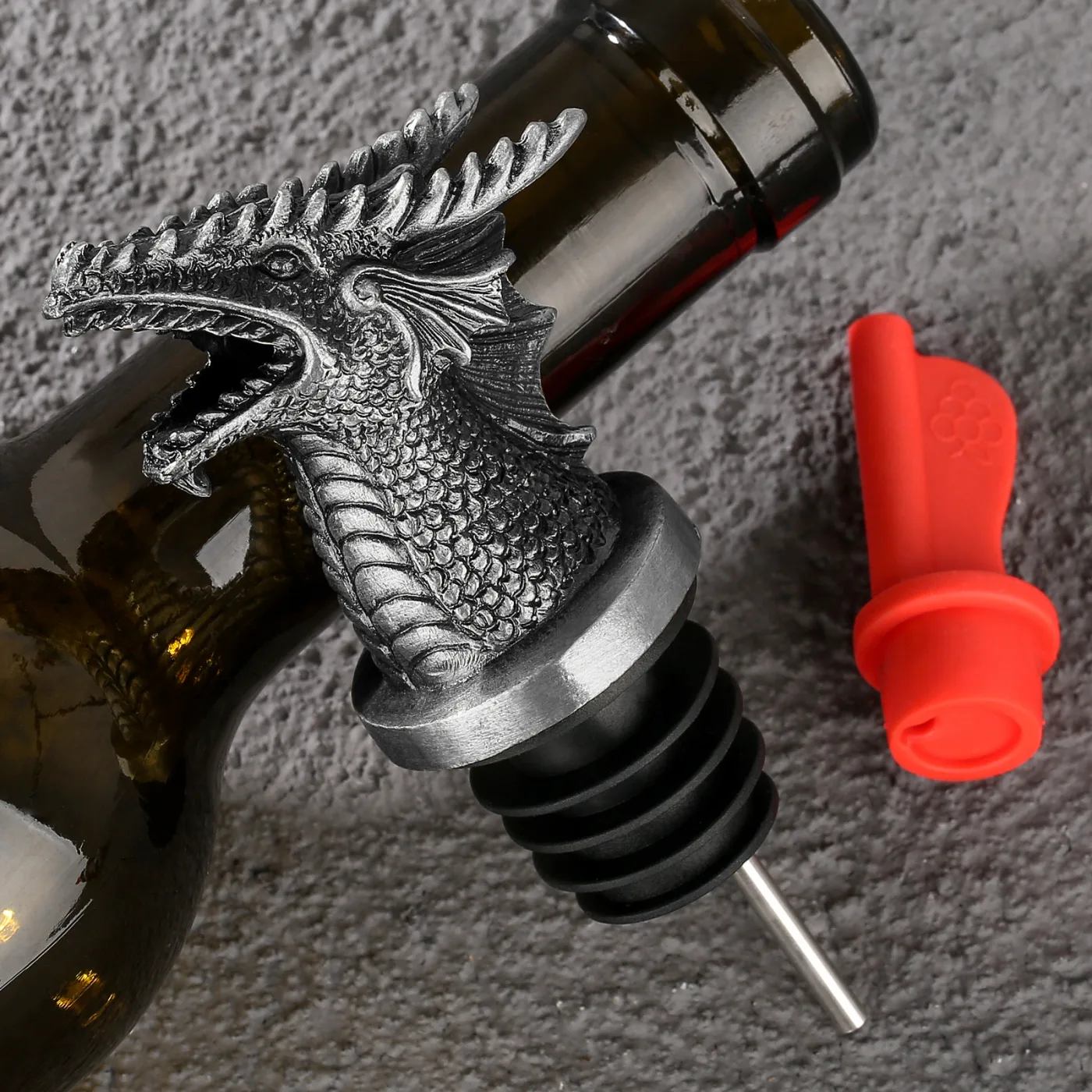 Silver dragon-head pourer on a dark bottle with the red silicone flow tip beside it