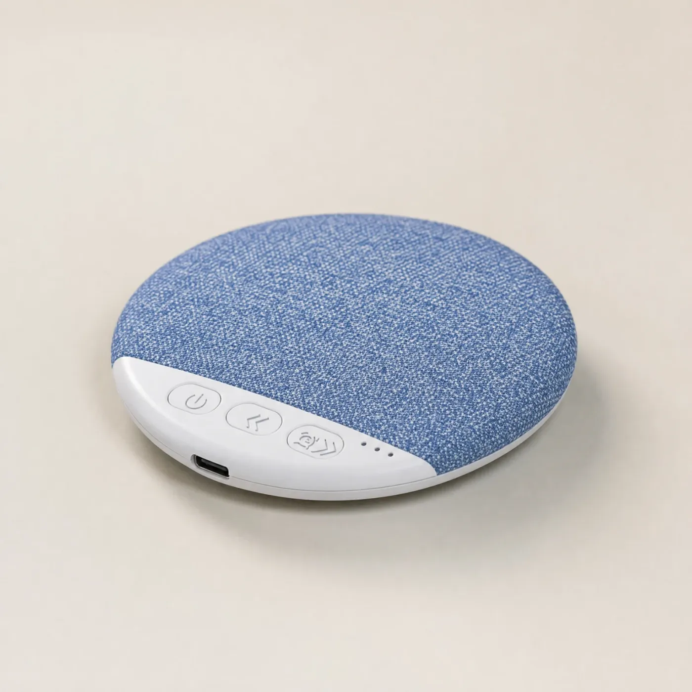 Round, thin pillow speaker with a blue fabric top and a white edge with three buttons, three small lights and a USB-C port