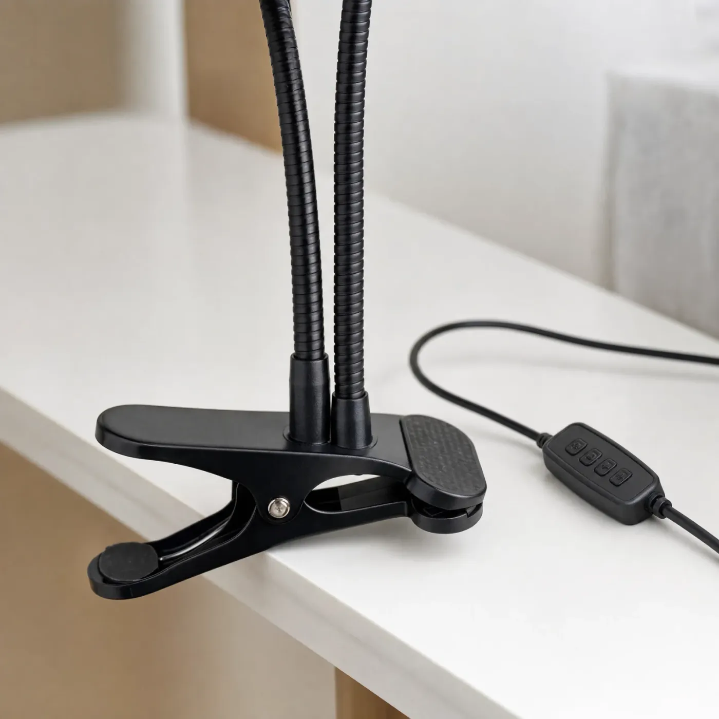 Close-up of the black spring clamp gripping a desk edge, the base of both bendable arms and the inline button controller