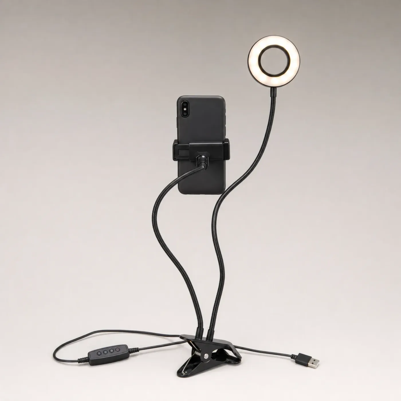 Black clip-on ring light lit white, with a phone in the holder on its second arm, the clamp at the base and the USB cable and button controller