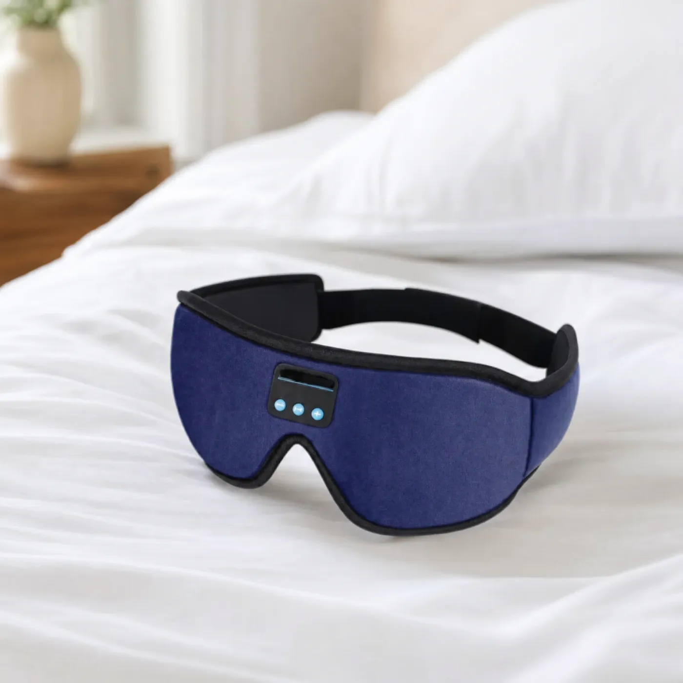 Dark blue Bluetooth sleep mask with a black trim and strap, lying on a white bed
